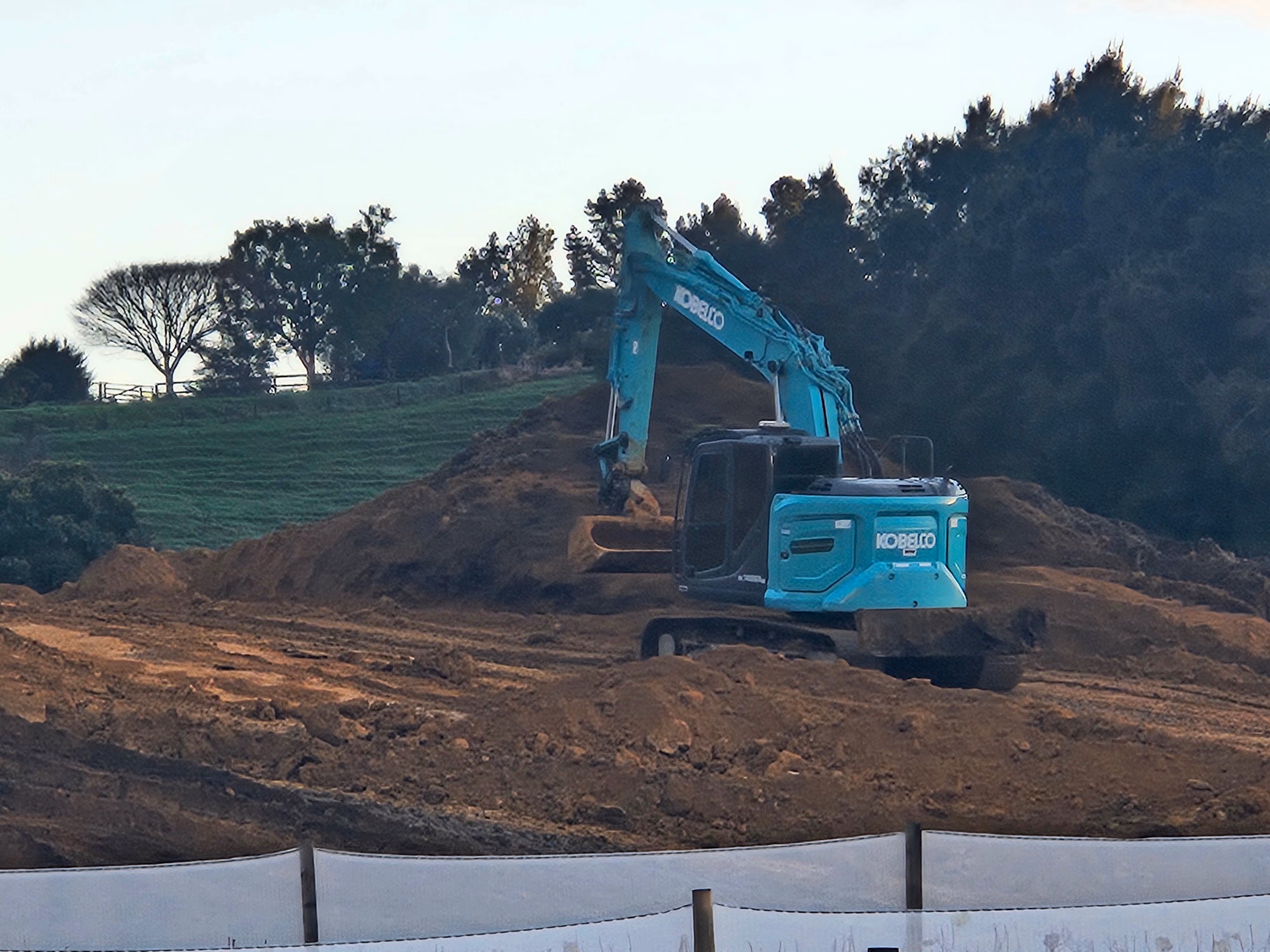 Excavator working a bulk earthworks cut above orchard netting