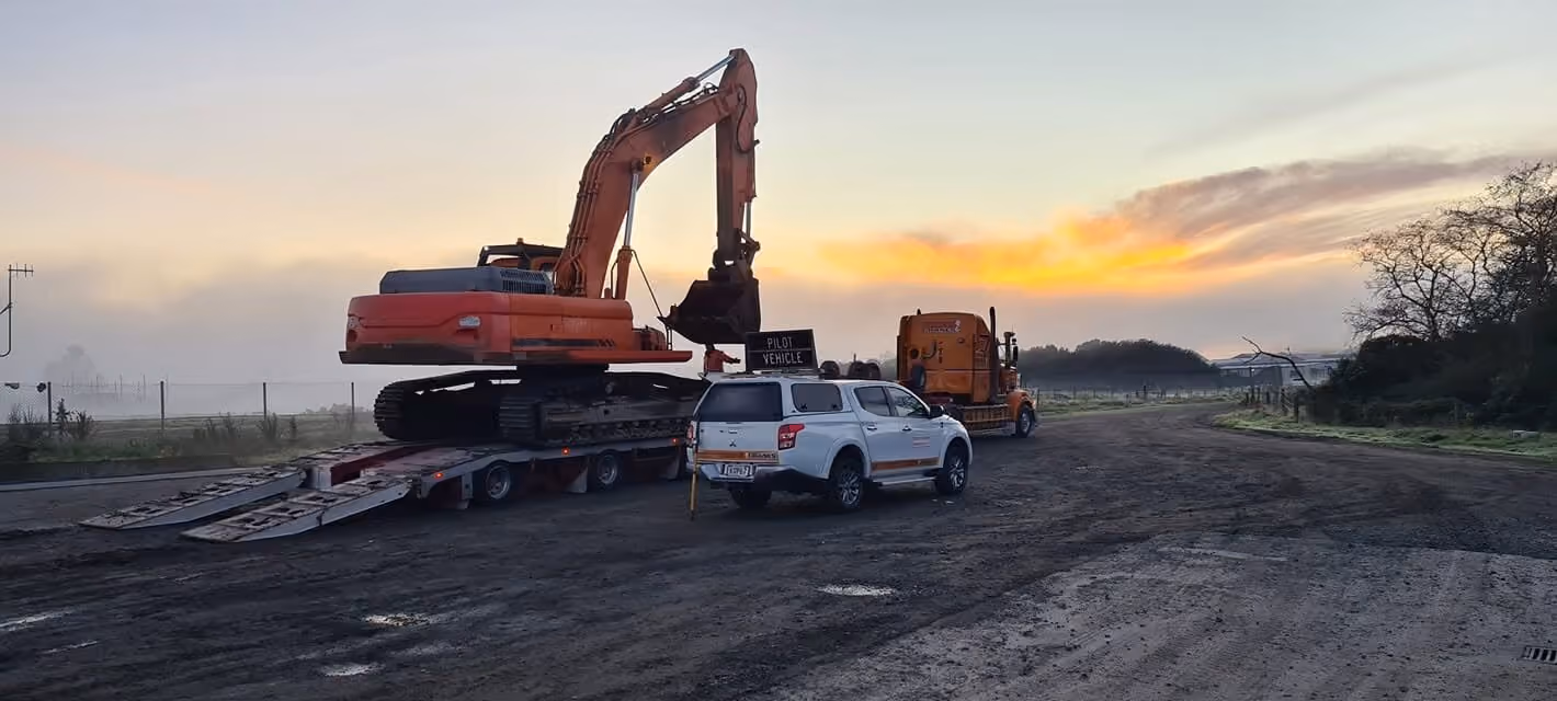 Excavator on a transporter with a pilot vehicle at sunrise