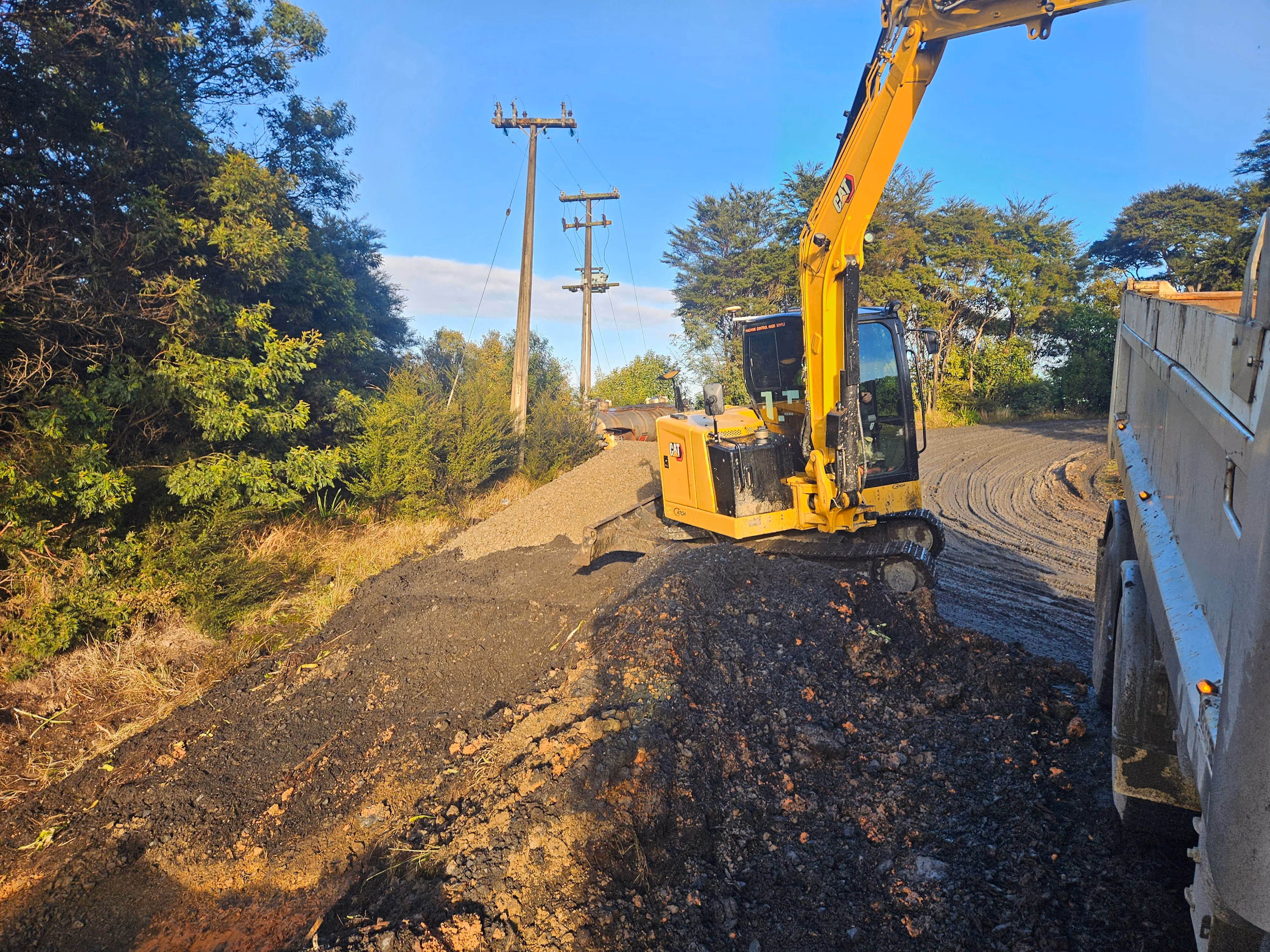 Excavator spreading base course along a rural road